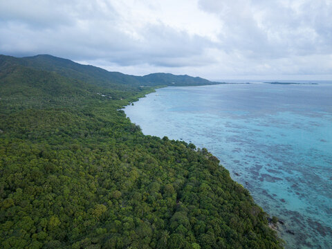 Aerial view of verdant forests meet the turquoise sea along the Tanjung Gelam Beach under a cloudy sky, Karimunjawa, Central Java, Indonesia.
