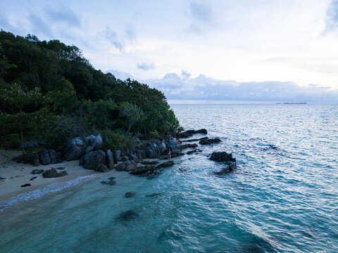 Aerial view of turquoise waters meet the rocky shore and lush greenery of Tanjung Gelam Beach, Karimunjawa, Central Java, Indonesia.