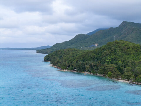 Aerial view of the turquoise waters meeting the lush green forests along Tanjung Gelam Beach under a cloudy sky, Karimunjawa, Central Java, Indonesia.