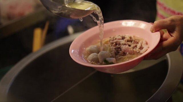 Close up shot a noodle vendor pouring broth and boiled winter melon into a bowl at a Thai noodle shop
