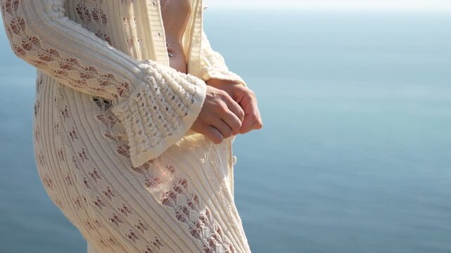 Woman, beach, ocean, young woman in a white knitted cardigan unbuttons to reveal her leopard print bikini by the sea on a sunny day