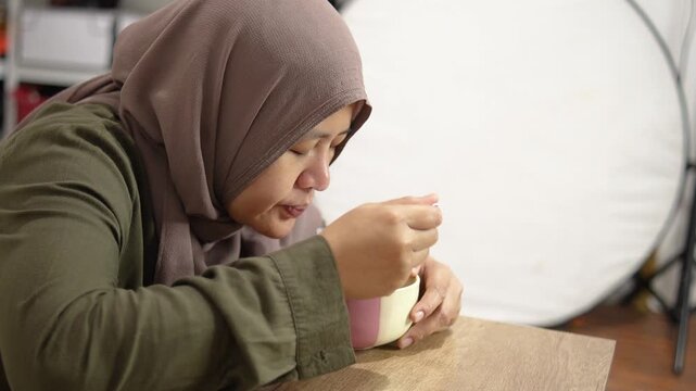 Mature Asian woman in hijab eating instant noodles from a bowl alone in her bedroom. Muslim lady enjoying hot spicy ramen at home