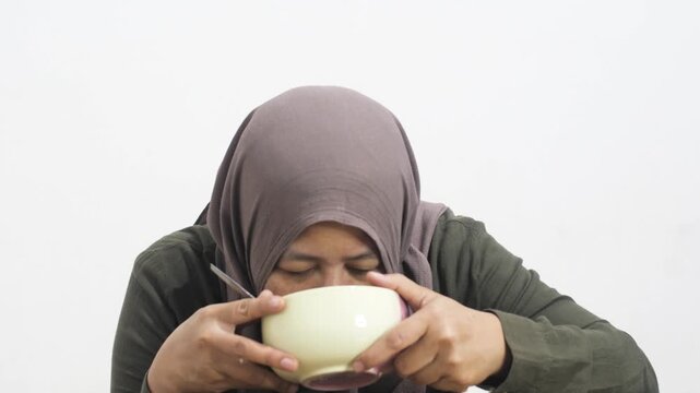Mature Asian woman in hijab eating instant noodles from a bowl alone in her bedroom. Muslim lady enjoying hot spicy ramen at home