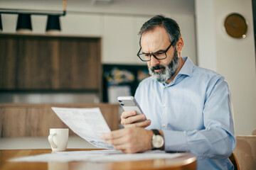 Man managing home finances, reviewing documents and using smartphone