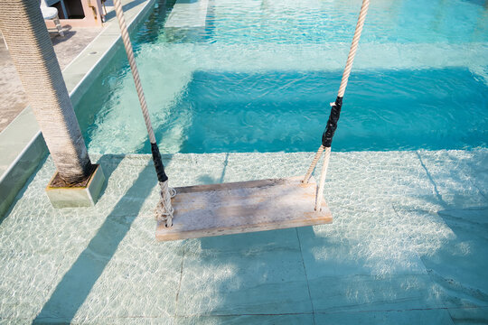 The serene scene of a wooden swing suspended above a crystal-clear swimming pool, inviting relaxation and leisure.