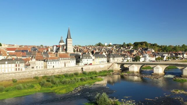 Aerial view of the picturesque town of La Charite sur Loire with its historic stone bridge spanning the Loire River under a clear blue sky.