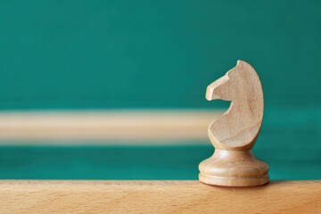 A light wooden knight chess piece stands on a wooden edge against a blurred green background. Concept of tactical thinking. © Helga P-A.