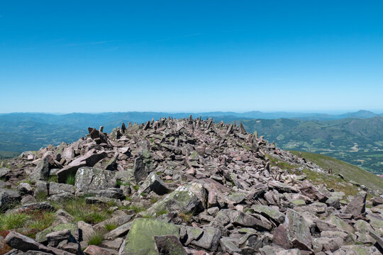 Cume rochoso do Monte Autza sob um c&eacute;u azul l&iacute;mpido, com um vasto panorama de montanhas verdejantes dos Piren&eacute;us franceses ao fundo