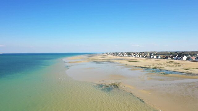 Wide aerial shot of Juno Beach at low tide with clear blue sky and coastal houses in Bernieres sur Mer, Normandy, France.