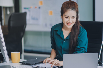 Determined asian businesswoman works late in a modern office, confidently analyzing data on her...