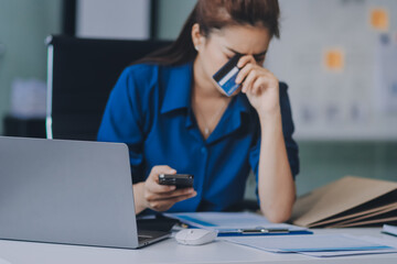 Fototapeta premium Young businesswoman is holding two credit cards with a worried expression, trying to decide which one to use to pay off her debt