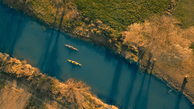 Aerial view of two kayakers on a serene, winding river surrounded by lush greenery and autumn foliage. Captures adventure and tranquility, ideal for travel and sports enthusiasts.
