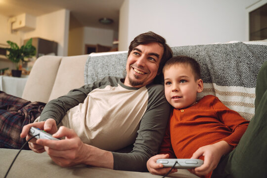 Father and son playing videogames together at home on the sofa