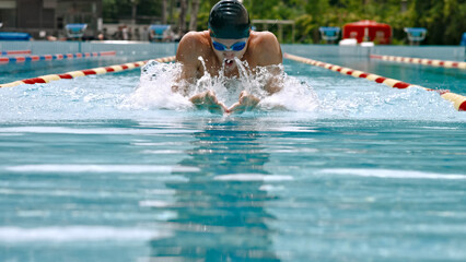 A swimmer dives into a pool, performing a powerful swimming stroke. The swimmer, wearing a cap and goggles, is focused on their stroke in a competitive pool setting.
