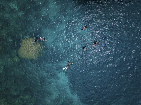 Aerial view of snorkelers floating in the crystalline turquoise waters near a vibrant coral reef, creating a stunning contrast of blues, Karimunjawa, Central Java, Indonesia.