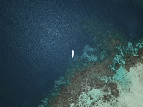 Aerial view of a lone boat adrift on the deep blue sea contrasting with the vibrant turquoise shallows near the coral reefs, Karimunjawa, Central Java, Indonesia.