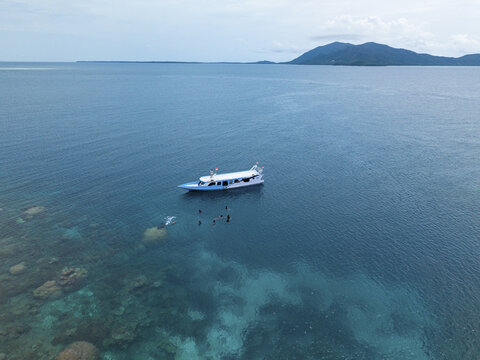 Aerial view of a boat floating on the turquoise waters of the Java Sea, with snorkelers exploring the vibrant coral reefs, Karimunjawa, Central Java, Indonesia.