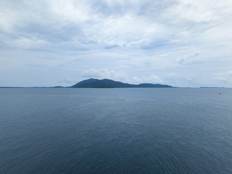 Aerial view of the shimmering ocean stretching to the horizon under a cloudy sky, with a distant island silhouette, Karimunjawa, Central Java, Indonesia.