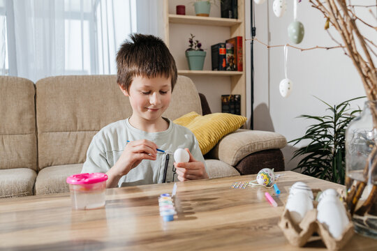 Boy decorating Easter egg with marker at home during spring holiday