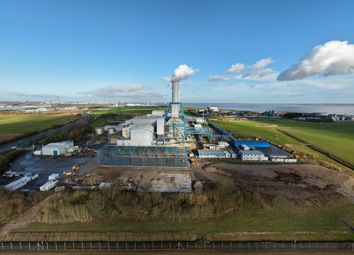 Aerial view of the South Humber Bank Power Station with its dominant chimney stack releasing a plume against a vibrant blue sky, Grimsby, United Kingdom.