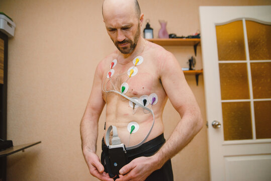 Middle-aged Man with Holter Monitor Electrodes Attached to Chest for Heart Rate Monitoring at Home