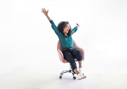 Confident woman smiling and raising arms sitting in chair indoors