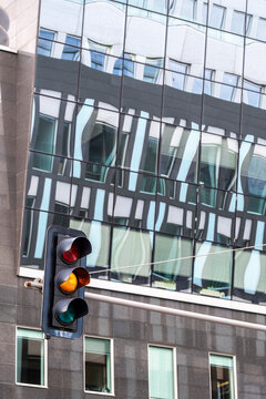 Modern urban street scene with traffic signal beside glass building facade windows and reflection in daylight showing contemporary architecture geometry and city control detail