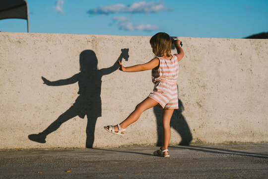 Child playing with shadow and dancing outdoors in sunlight