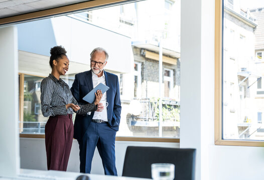Colleagues communicating and smiling with tablet in modern office
