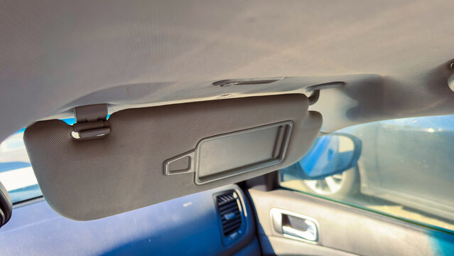 Sun visor located inside a vehicle's cabin, showing the mirror part above the front seats, during daylight hours with sun light coming through the front windows