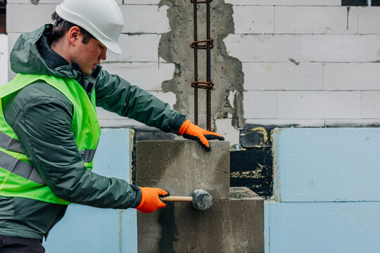 Builder in hard hat and vest leveling bricks at construction site