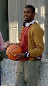 Vertical video: Leaning man in yellow coat shifting at low wall angling basketball as peer reaching