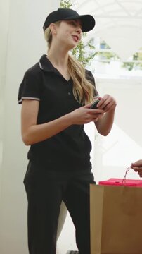 Vertical video: Smiling courier in black polo offering phone to customer wrist at door confirming
