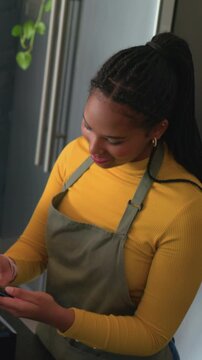 Vertical video: Replying offscreen call, woman in apron checking card-reader for payment at counter