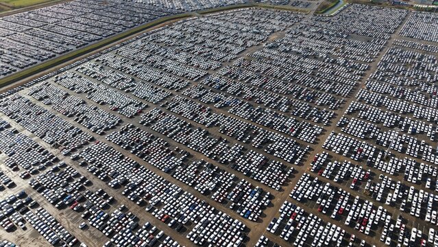 Aerial view of thousands of cars parked in a vast lot, reflecting sunlight in ordered rows, creating a sea of metallic hues, Grimsby, United Kingdom.