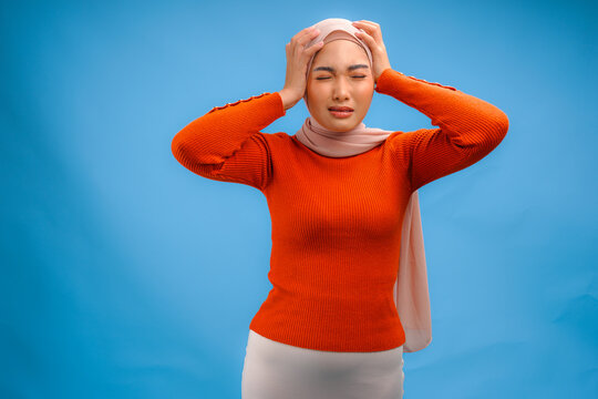 Stressful young Asian Muslim woman in a hijab is looking confused and having headache.