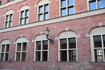 Obraz premium Historic red brick building facade with rounded window shutters and vintage wall lantern 
