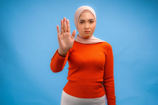 Beautiful Asian Muslim woman wearing a hijab with hand gesture posing rejection or stop.