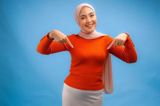 Smiling Asian Muslim woman wearing hijab pointing to the copy space below her.