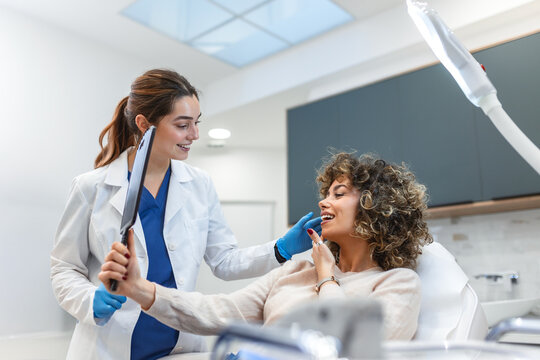 Patient looking at results in mirror. Facial treatment, Healthcare And Medicine concept. Attractive smiling woman in clinic chair with female doctor in white coat. Professional aesthetic medical care.