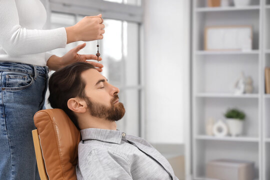 Female psychologist with pendulum hypnotizing man in office