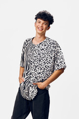 young man smiling wearing a black and white animal print shirt with casual black pants posing with...
