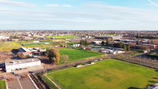 Drone shot over college sports and athletic fields in Sacramento, California during late afternoon. Applicable to education, sports facilities, and campus planning content. Rotating panning drone view