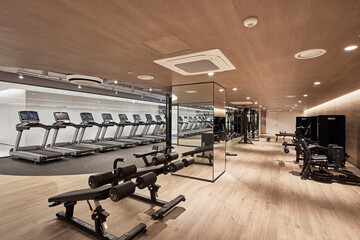 Empty modern fitness gym interior with cardio machines and strength training equipment.