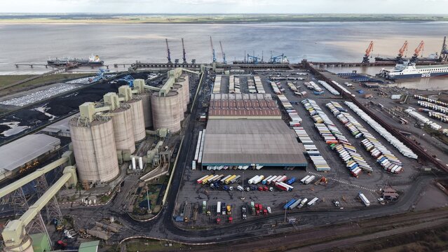 Aerial view of Immingham Dock, where colossal silos loom over rows of parked trucks, the scene framed by the somber hues of the Humber Estuary, Immingham, England, United Kingdom.