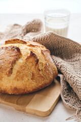 Golden sourdough loaf on wooden board with knit Linen Towel and glass of milk. Ideal for culinary, baking, and food lifestyle content.