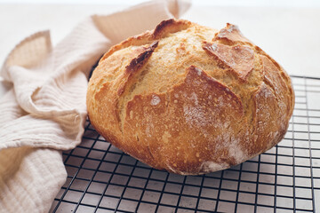 Round sourdough loaf resting on black wire cooling rack with beige linen towel. Perfect for baking, food blogs, and culinary projects