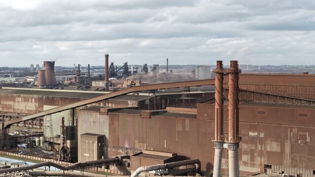 Aerial view of a sprawling industrial complex with towering chimneys and metallic structures under a vast, cloudy sky, Scunthorpe, United Kingdom.