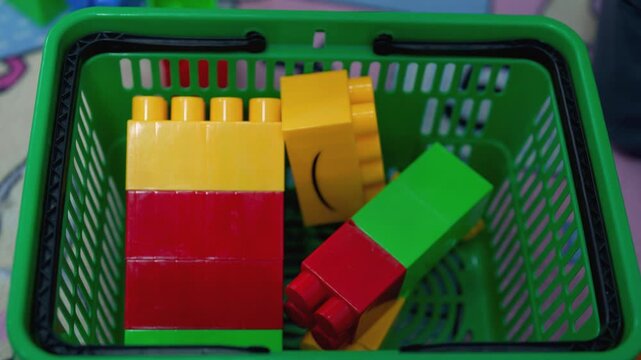 Colorful building blocks in a green basket for children. A group of children enjoys stacking and organizing bright building blocks in a green basket on the floor of a playroom.