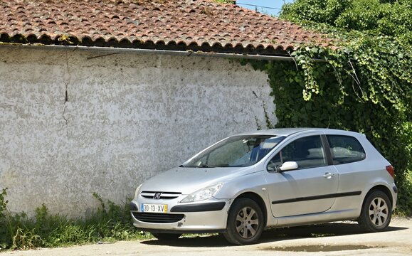 Silver Peugeot 307 hatchback parked by old building wall